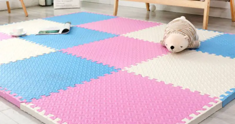 Pink, white, and blue puzzle mat with a stuffed bear on it.