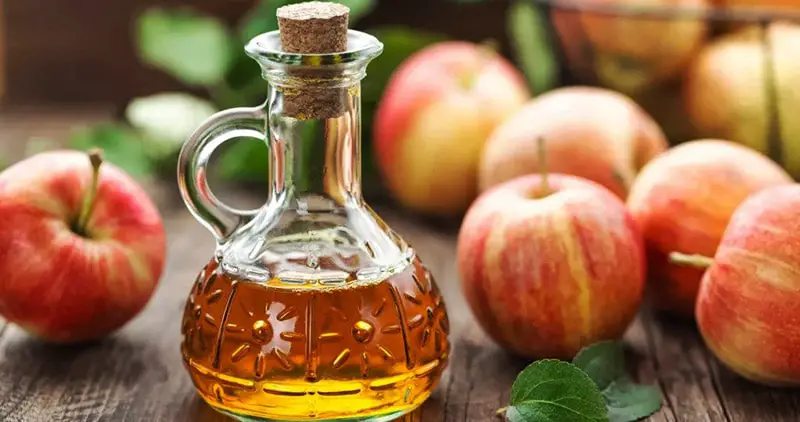 Bottle of apple cider vinegar next to apples