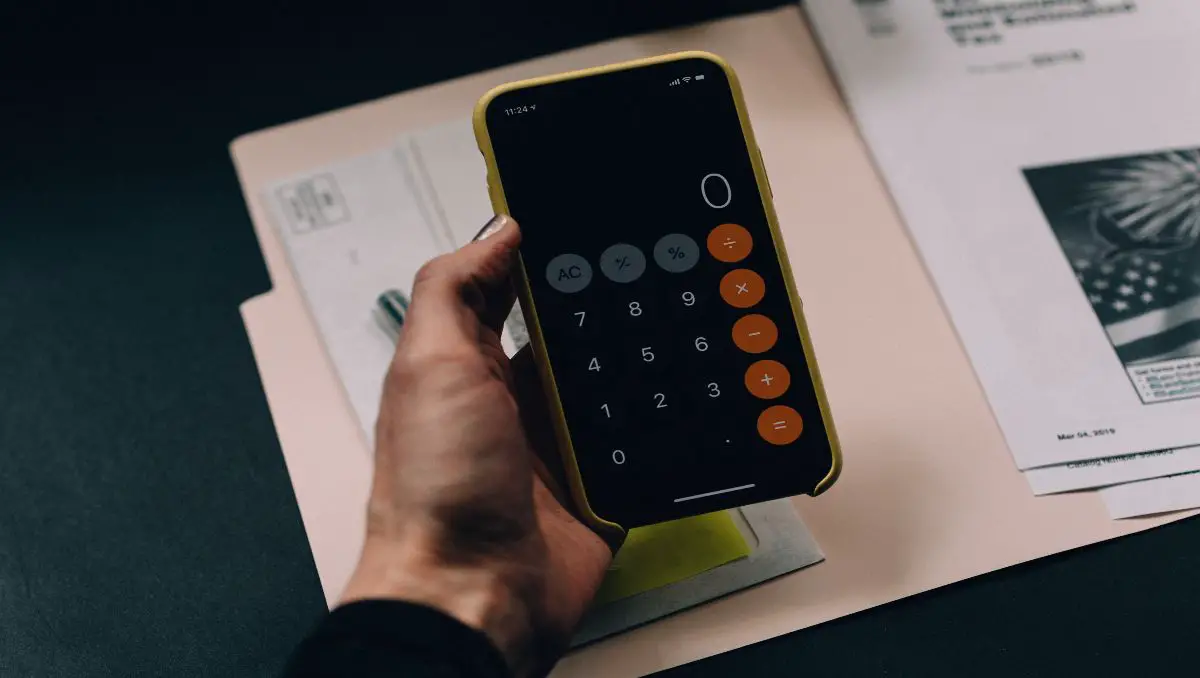 A hand holding a calculator while planning a budget. 