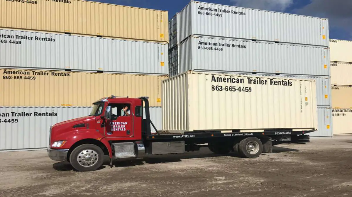 A truck carrying a large shipping container for rental.
