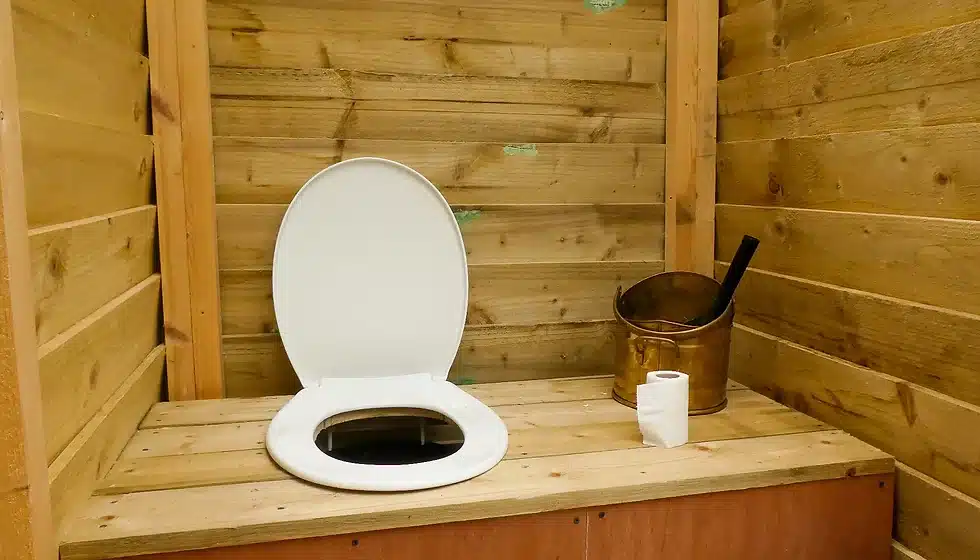 A composting toilet, a roll of tissue, and a bucket inside the bathroom of a tiny home. 