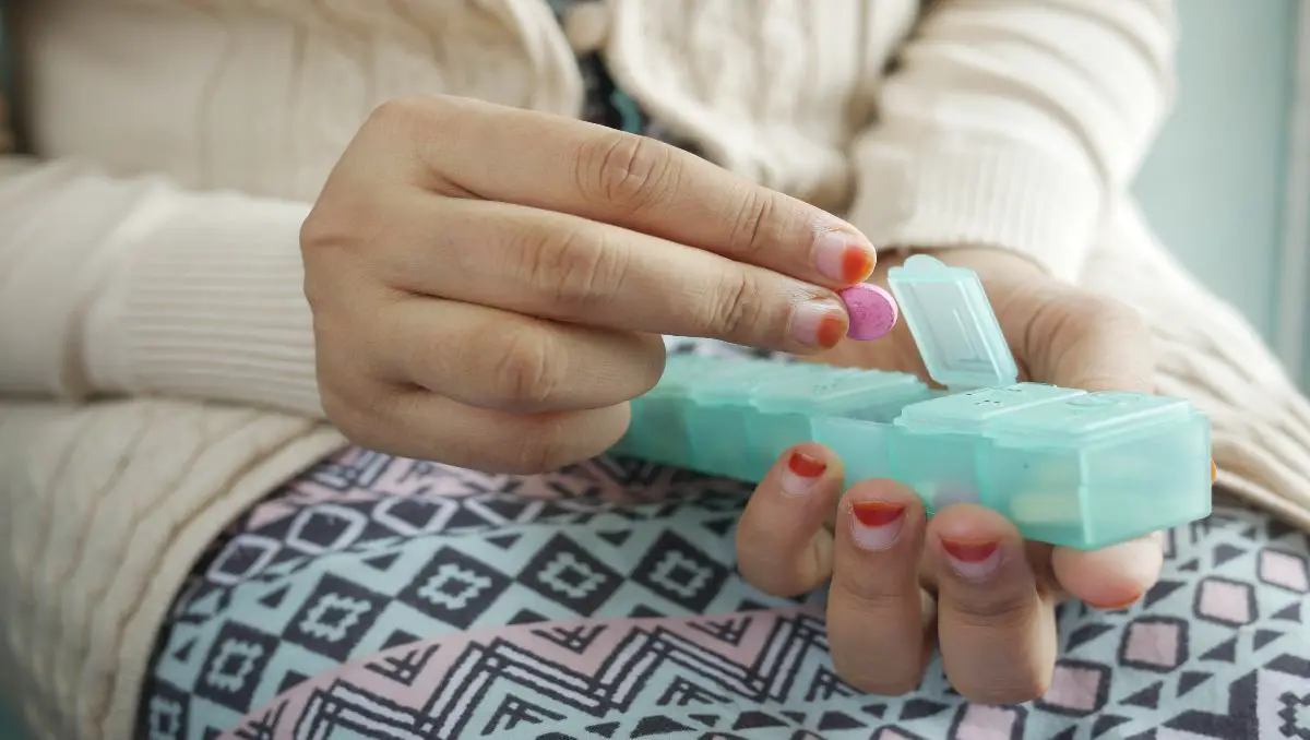 A pregnant woman putting a tablet on her mini pill organizer. 