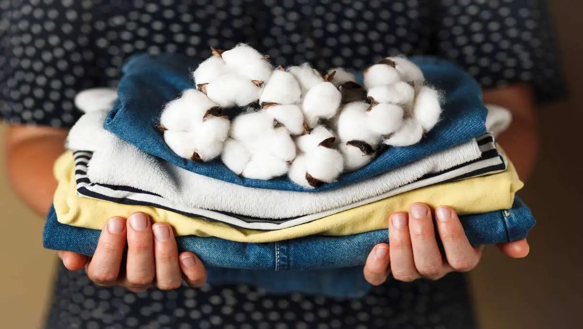 A woman holding a stack of clothes with cotton flowers on top of it.