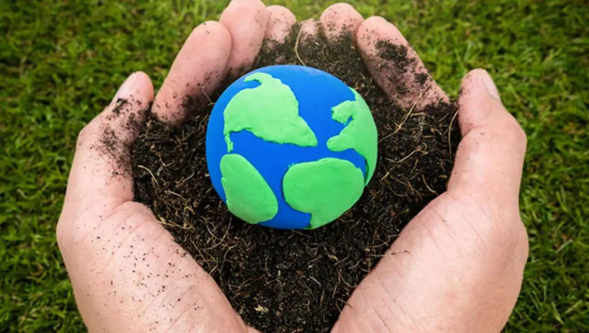 A hand holding a handful of soil with a small, blue and green clay globe in the middle.