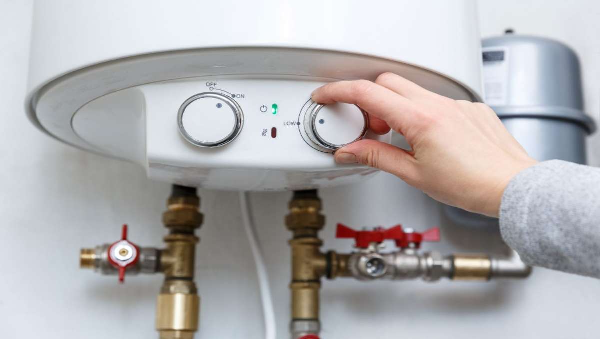 A hand adjusting the temperature of a water heater in a tiny house.