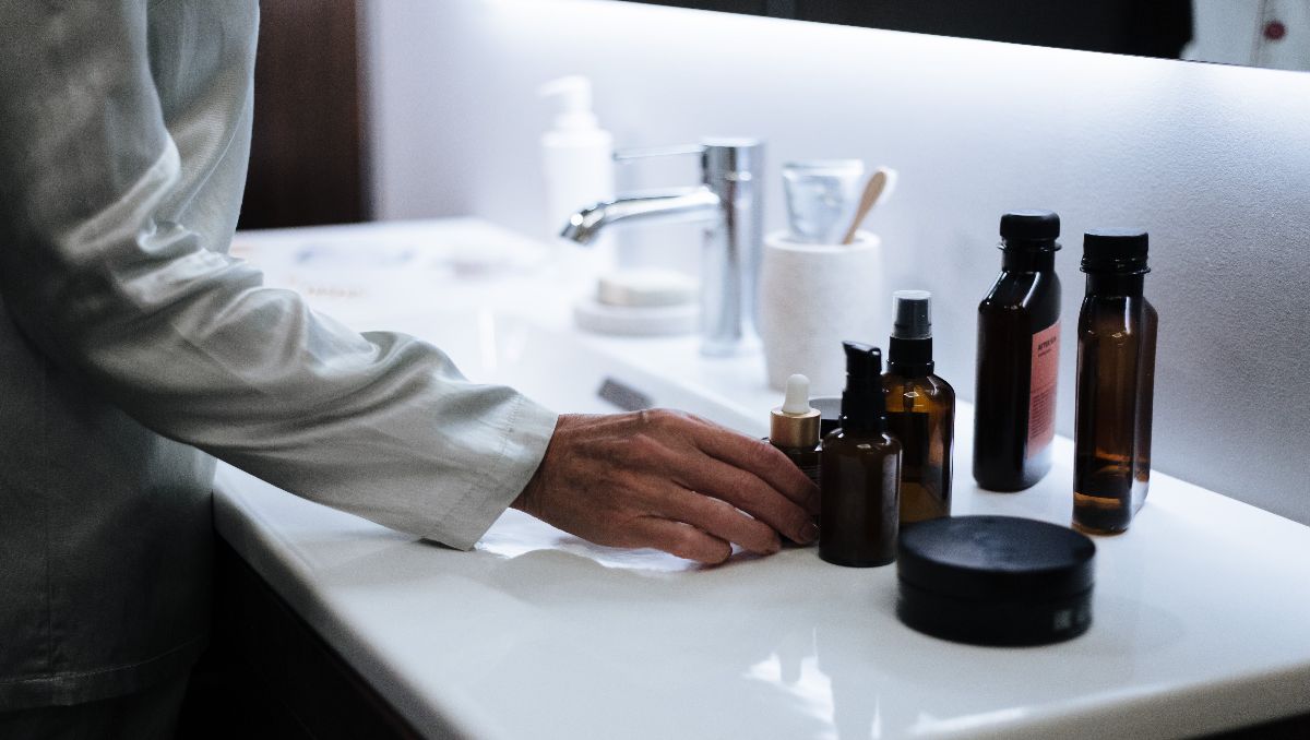 A woman in the bathroom holding a bottle of toner beside the other skincare products.