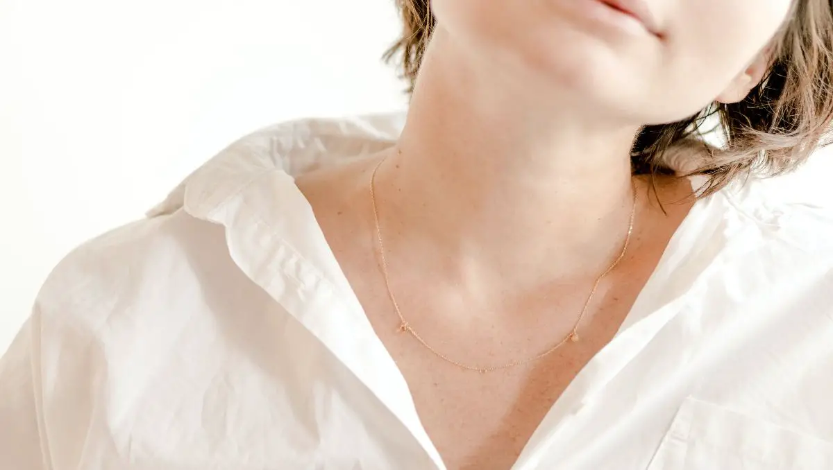 The neck of a female wearing white polo and gold necklace.