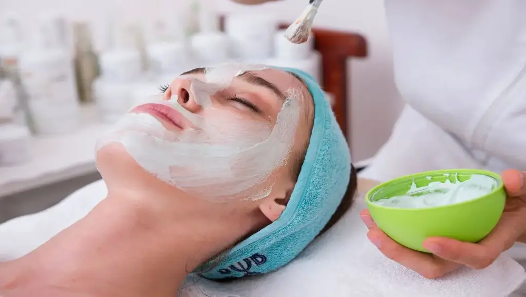 An aesthetician applying facial mask to the female customer.