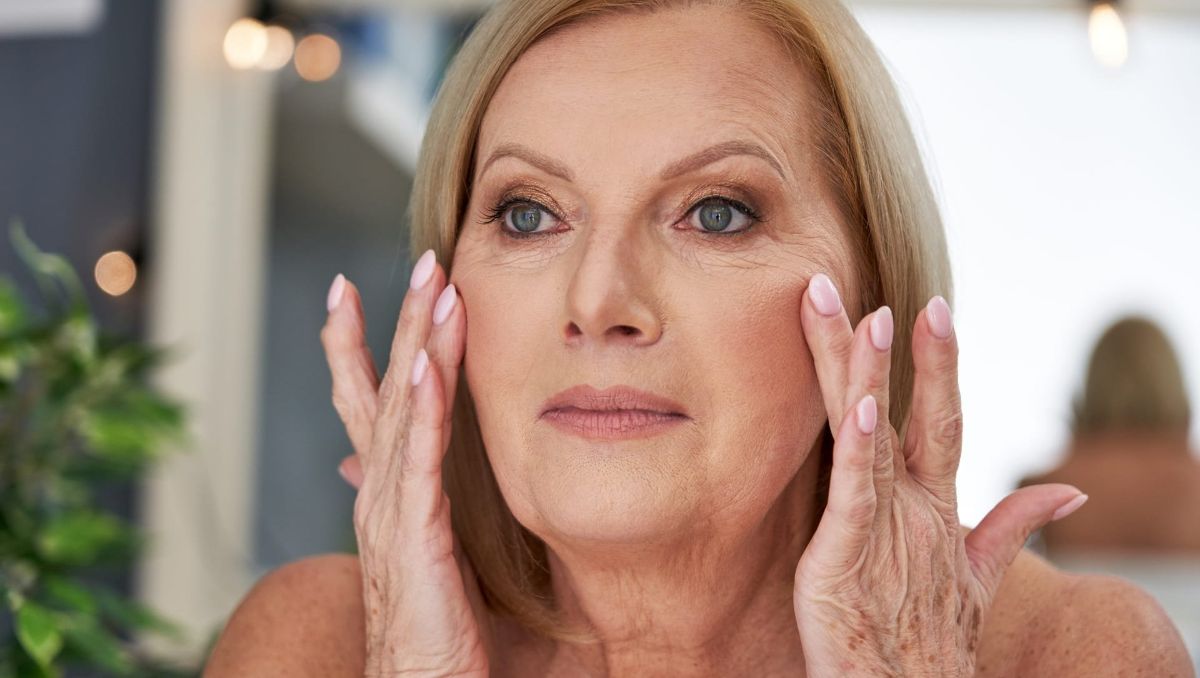 An older woman touching her face, pointing out wrinkles and fine lines.
