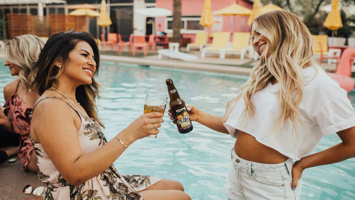 Two girls cheering drinks at the poolside.