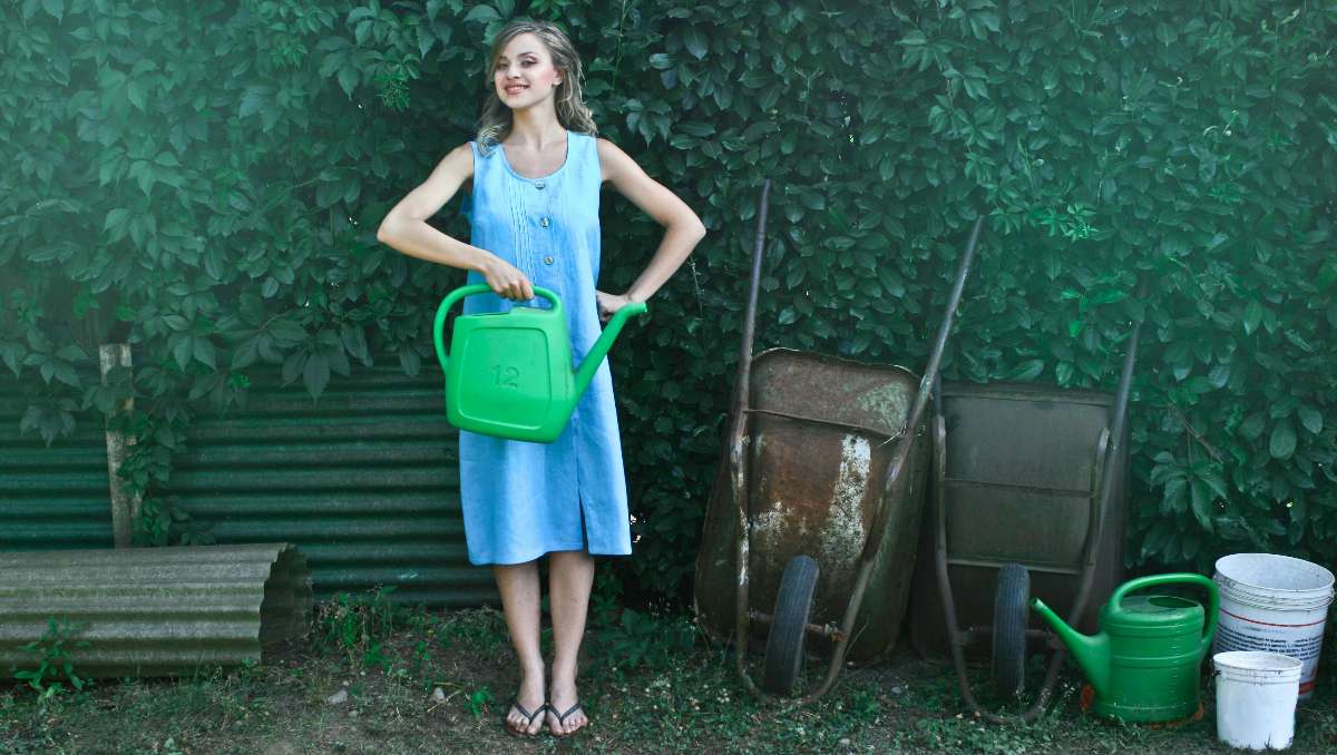 A young woman smiling and posing while holding a watering can.