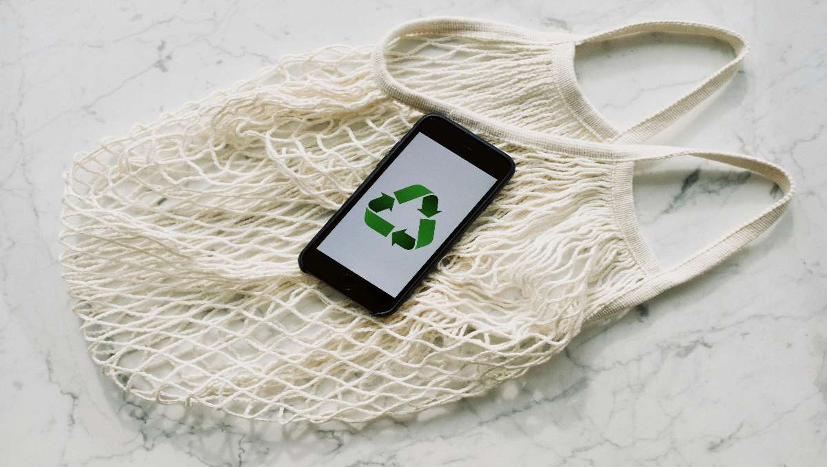A white mesh bag with smartphone placed on top with the recycling symbol.