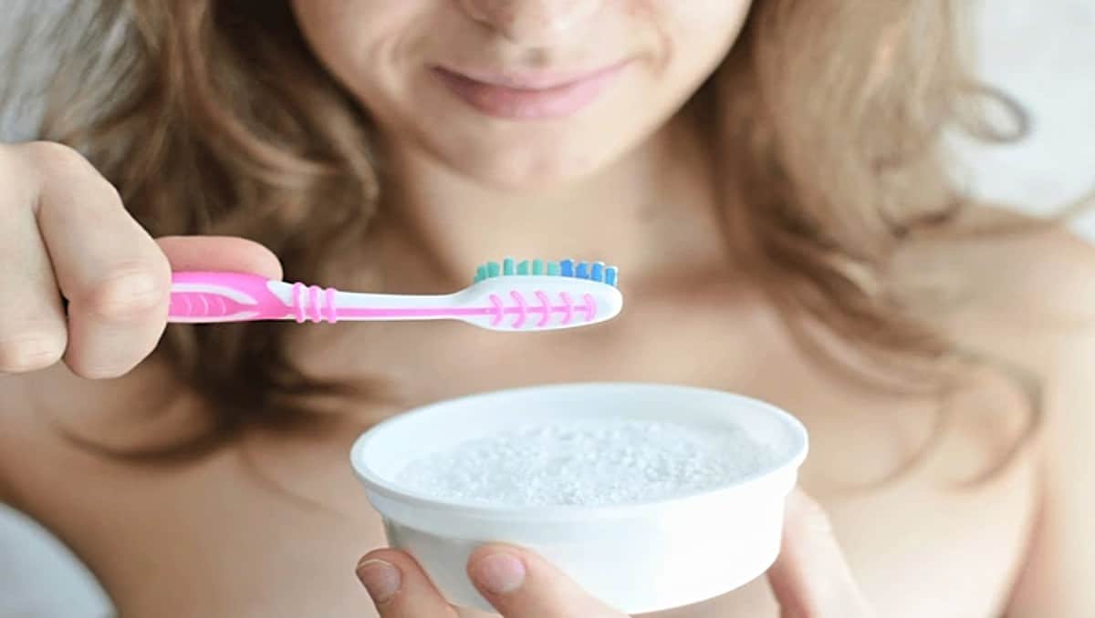 A young girl holding a toothbrush and a bowl of baking soda.